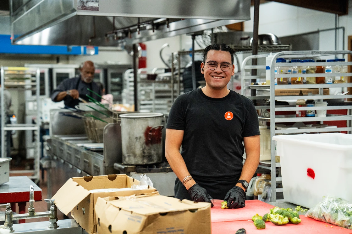 A Summer Camp Cooks chef in a branded shirt preparing fresh vegetables on a stainless steel prep counter